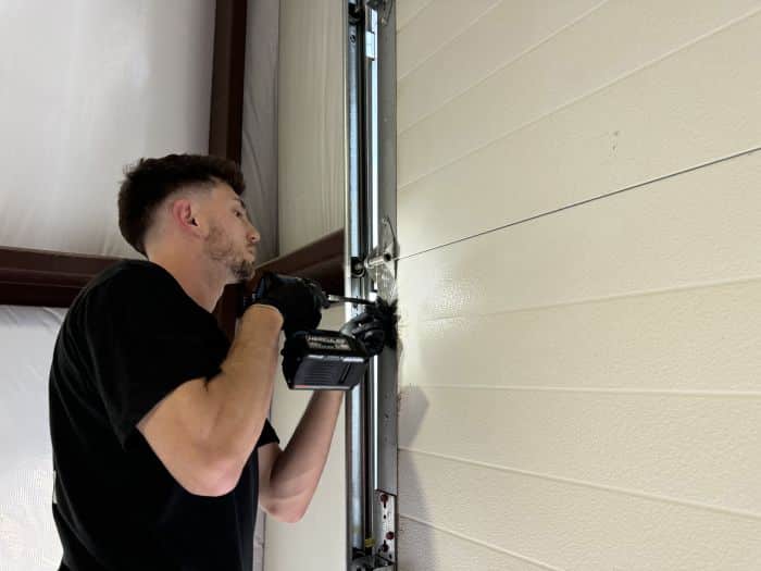 Garage door technician using a power drill on a garage door.